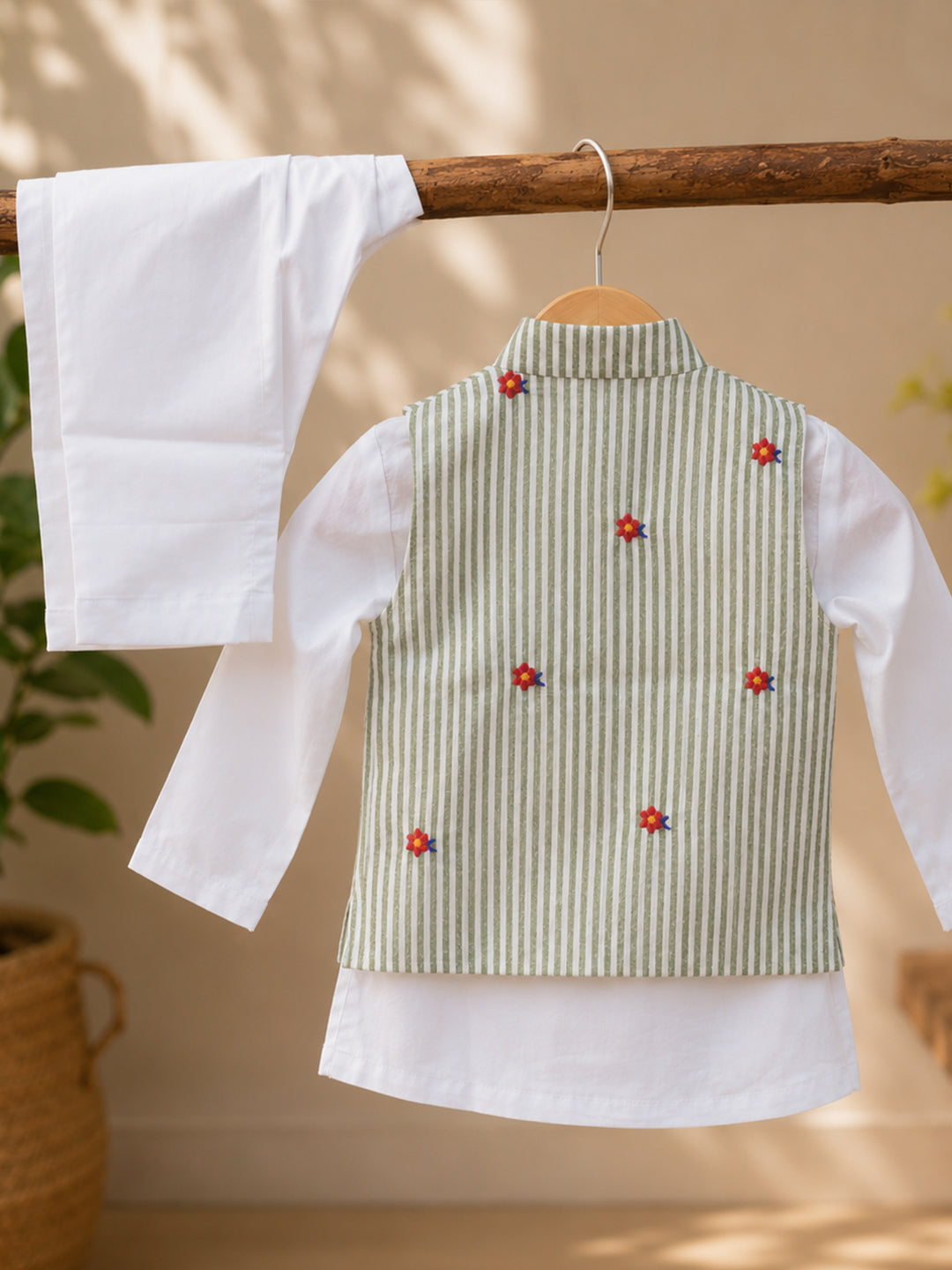 A children's traditional outfit hanging on a wooden hanger, featuring a white long-sleeve kurta and a sleeveless embroidered vest in light green and white vertical stripes with small red and blue floral motifs.