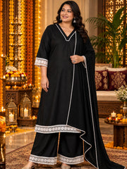 A woman modeling a black traditional Indian salwar kameez set with white embroidered borders, set against a warm, decorated festive background with marigold garlands and candles.